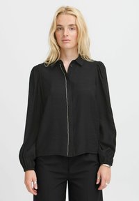Black long-sleeve blouse with a buttoned collar, featuring a textured fabric, puffed sleeves, and a central decorative stitching detail.