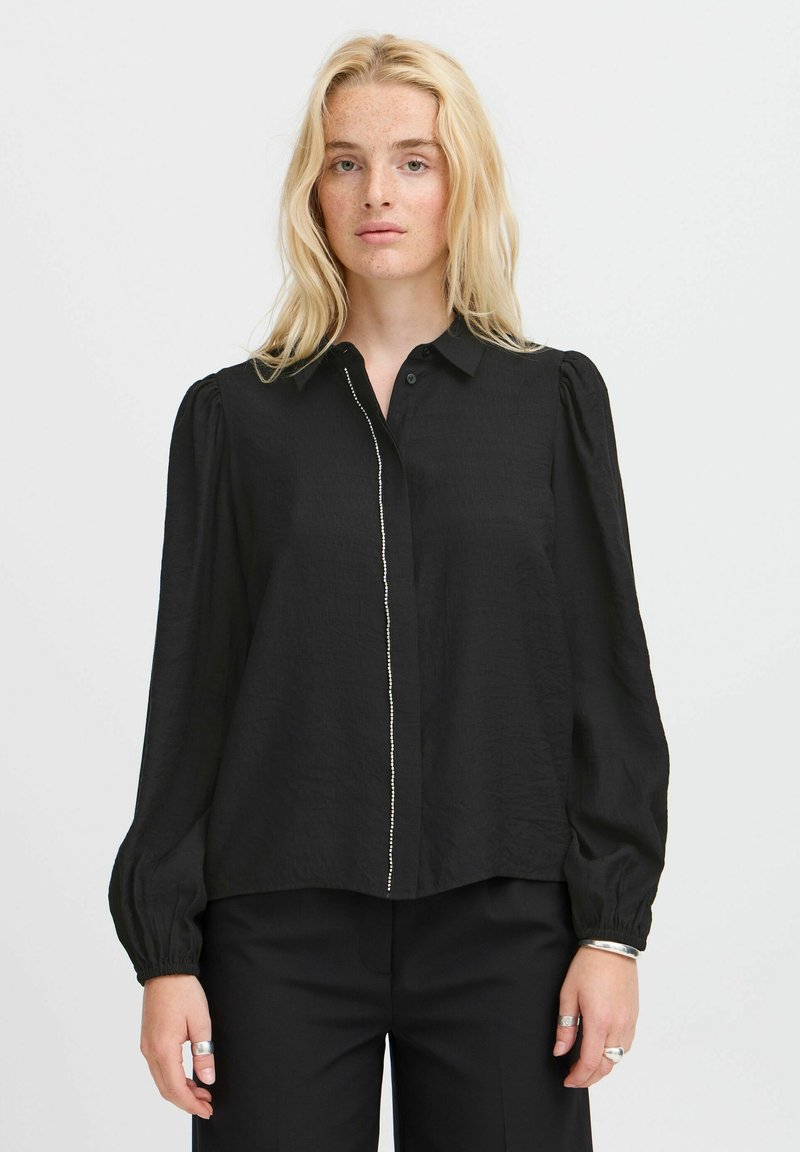 Black long-sleeve blouse with a buttoned collar, featuring a textured fabric, puffed sleeves, and a central decorative stitching detail.