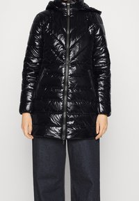 Czarna kurtka puchowa o błyszczącej, pikowanej teksturze, z kapturem, zamek błyskawiczny z przodu oraz dwoma bocznymi kieszeniami; długości do kolan z dopasowanym krojem.