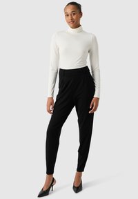 Maglione a maniche lunghe bianco con scollo a barco abbinato a pantaloni neri a sigaretta; vita alta, tessuto testurizzato, silhouette elegante, indossato con tacchi alti neri.
