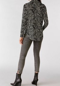 Schwarz-weiße Leopardenmuster Langarmshirt mit abgerundetem Saum, kombiniert mit grauen Skinny-Jeans mit seitlichen Reißverschlüssen und schwarzen Keilstiefeln.