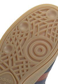 Suola della sneaker in gomma color beige chiaro; presenta una superficie testurizzata con motivi circolari e lineari. Include un logo in rilievo.