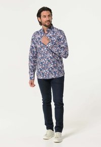 Bloemige overhemden in blauw, met witte, roze en paarse bloemen. Het materiaal heeft een gladde textuur; een slim-fit ontwerp. Draagt met donkere jeans en sneakers.