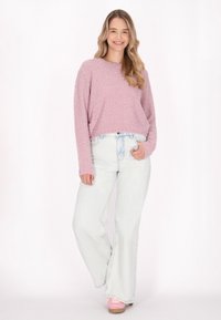 Pulover texturat de culoare roz deschis, cu mâneci lungi, purtat cu blugi deschis la culoare, ușor distruși, cu talie înaltă și adidași roz.