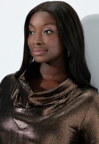 Metallisk brun topp med cowl-hals och hudliknande textur samt ett subtilt reptilmönster. Modellen har långt, rakt hår och guldörhängen.