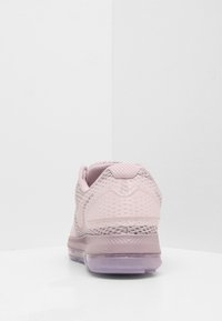 Zapatilla deportiva de color rosa claro con parte superior de malla, acentos texturizados y una suela púrpura translúcida. Presenta un talón redondeado y un branding mínimo.