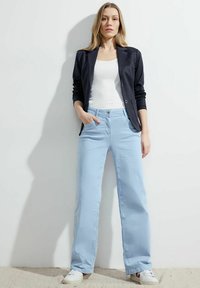 Blazer marine à deux boutons sur un débardeur blanc, associé à un pantalon large bleu clair et des baskets blanches. Tissu lisse et coupe classique.
