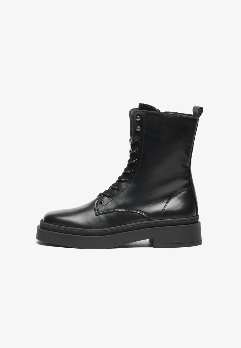Botas de tornozelo em couro preto com acabamento liso, sola plana, design de atacadores e ilhós de metal. Possui uma alça na parte de trás.