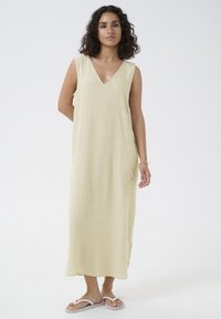 Robe maxi sans manches à rayures, en V, de couleur jaune pâle et blanche. Tissu doux avec une coupe ample et des poches latérales. Portée avec des tongs.