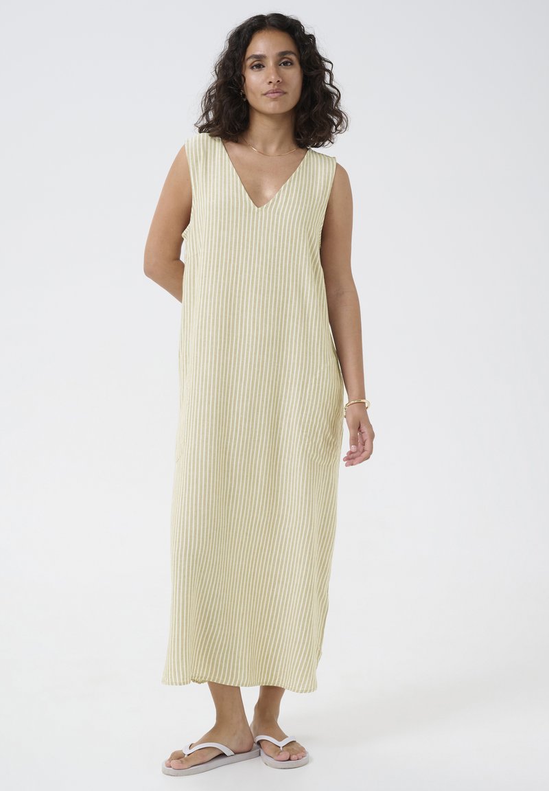 Robe maxi sans manches à rayures, en V, de couleur jaune pâle et blanche. Tissu doux avec une coupe ample et des poches latérales. Portée avec des tongs.