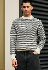 Maglione a maglia con un motivo a strisce bianche e nere, collo a girocollo a coste e polsini, abbinato a jeans in denim scuro.