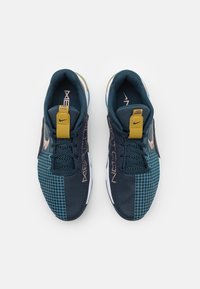 Mörkblå sportskor med nät- och rutmönster, med en gul rem, svarta skosnören och vit sula. Nike-logotyp på sidorna.