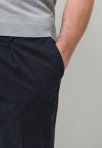 Maglione grigio a maglia con orlo a coste, abbinato a pantaloni blu navy con tasca laterale. Inquadratura ravvicinata dalla vita in giù, che mostra materiali testurizzati.