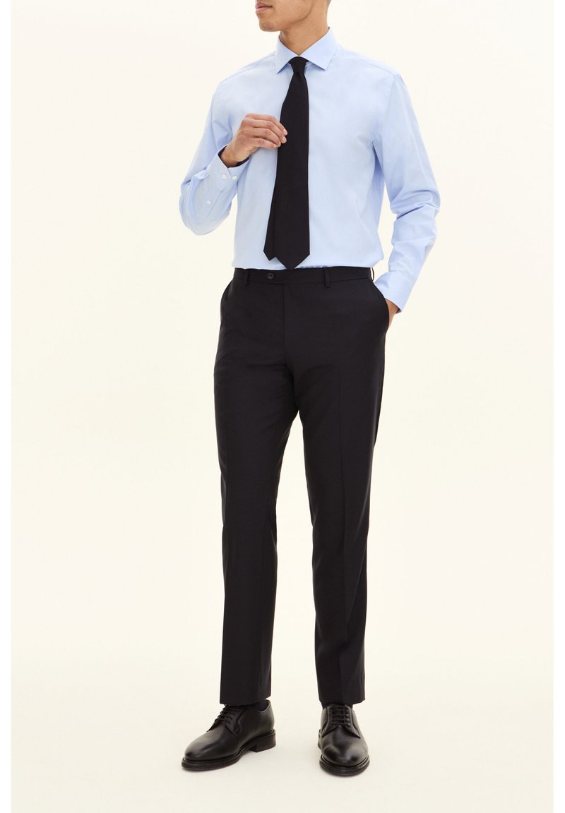 Lichtblauw overhemd met lange mouwen, zwarte stropdas en slim-fit donkere broek. Zwarte leren schoenen maken de formele outfit compleet.