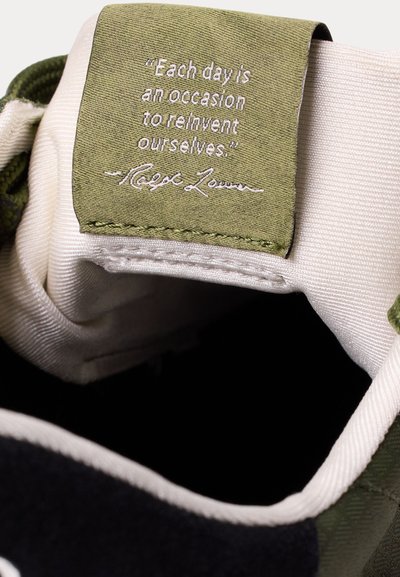 Citata „Kiekviena diena yra proga iš naujo atrasti save.“ Ralfo Laureno žalia audinio etiketė viduje smėlio ir juodo batų apykaklės.