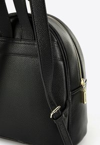 Černá kožená kabelka s texturovaným povrchem, zaobleným tvarem, dvojitými uchy a zlatým zipem s dekorativní štítkem.