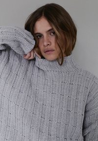 Szary gruby sweter dziany z wysokim kołnierzem, z pionowym prążkowaniem i subtelną fakturą. Rękawy są lekko oversize'owe.
