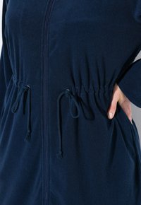 Námořnická modrá fleecová bunda na zip s elastickým stahovací pasem a bočními kapsami. Měkká textura a dlouhé rukávy. Minimalistický design.