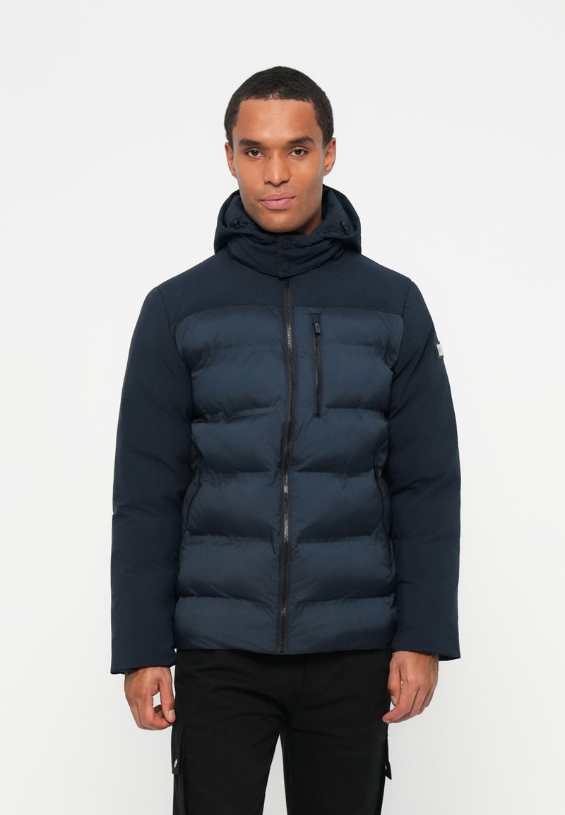 Tumesinine puffer jope kapuutsiga, millel on lukuga esirihm, tikitud tekstuur ja küljetaskud. Mustad detailid.