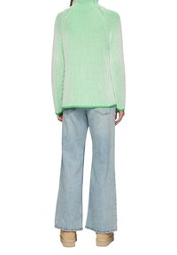 Grün-weißer gerippter Pullover mit hohem Kragen, kombiniert mit hellblauen weit geschnittenen Jeans und beigen Slippers.