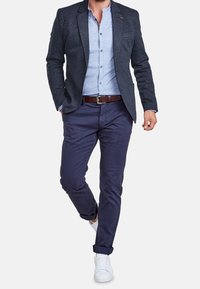 Marinblå kavaj i texturerad tyg, ljusblå skjorta, marinblå chinos och vita sneakers. Brun läderbälte som en anmärkningsvärd detalj.