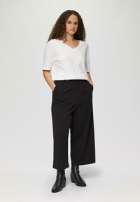 Witte V-hals shirt, zwarte wijde broek en zwarte enkellaarzen. Gladde stof en relaxed fit, met zakken in de broek.