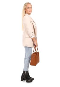 Lichtbeige blazer met opgerolde mouwen, witte top, lichtblauwe jeans, zwarte enkellaarsjes en een bruine leren handtas.