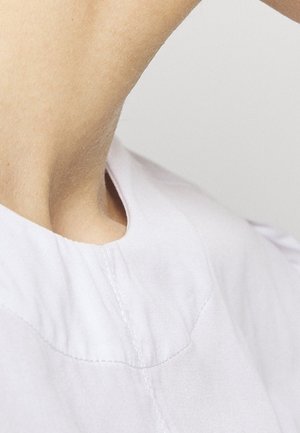 Gros plan sur le cou et l'épaule d'une personne portant un vêtement blanc avec des coutures visibles près de l'encolure.