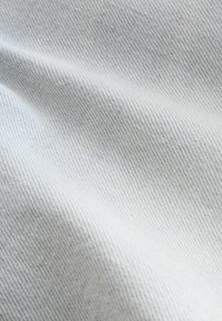 Gros plan d’un tissu gris clair, tissé de manière serrée, avec des plis doux et une texture de fil diagonale visible.