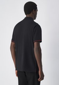Zwarte poloshirt met een kraag, voorzien van rode accentstiksels op de mouwen. Glad textuur, korte mouwen en een rechte zoom.
