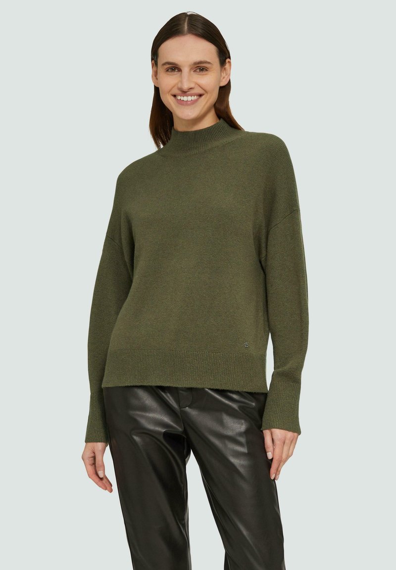 Olivgrüner Pullover mit hohem Kragen und überschnittenen Schultern, mit einem gerippten Saum und Bündchen, kombiniert mit schwarzen Lederhosen.