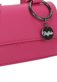 Borsa fucsia con superficie liscia, forma tondeggiante e hardware nero. Presenta un portachiavi circolare e un'etichetta nera brandizzata.
