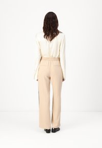 Beige wijde broek met een elastische tailleband, gecombineerd met een crèmekleurige zijden blouse. Heeft een zachte textuur en een getailleerd ontwerp.
