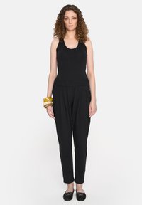 Czarny top na ramiączkach i luźne, zwężające się spodnie wykonane z miękkiego materiału. Wyraźna elastyczna talia i stos bransoletek w różnych kolorach.