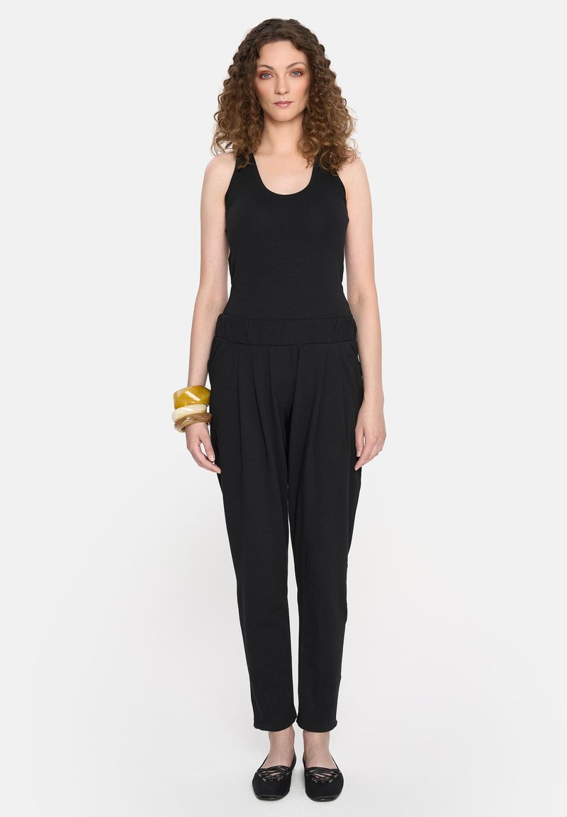 Czarny top na ramiączkach i luźne, zwężające się spodnie wykonane z miękkiego materiału. Wyraźna elastyczna talia i stos bransoletek w różnych kolorach.