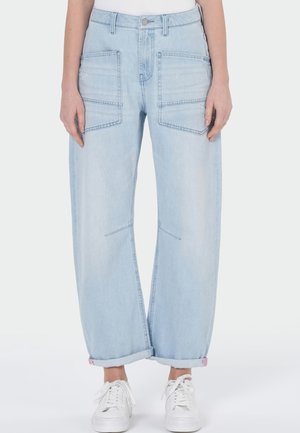 Hellblaue Jeans mit weitem Bein und großen Vorderhosentaschen, umgeschlagene Säume, kombiniert mit weißen Sneakers und einem weißen Top.
