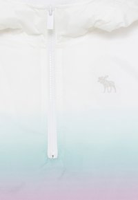 Bílá bunda se zipem vpředu, s gradientním přechodem od modrozelené k levandulové. Na boku se nachází stříbrná vyšitá nášivka losa.