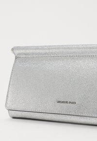 Silverfärgad kuvertväska med glittrig finish, rektangulär form och klaffstängning. Har präglad "MICHAEL KORS"-logotyp. Slät textur.
