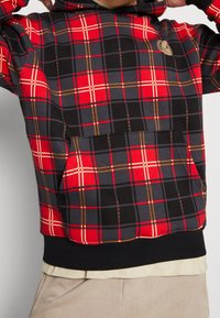Sudadera con capucha de cuadros rojos y negros, con un bolsillo frontal, textura suave, capucha con cordón y dobladillo acanalado negro. Logo en dorado en el pecho.