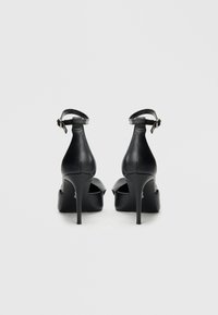 Schwarze High-Heels mit glattem Lederfinish, Knöchelriemen und offenem Zehendesign. Ausgestattet mit einem Stiletto-Absatz und Plateau-Sohle.