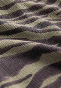 Tarnstoff in Schattierungen von Grün und Schwarz mit wellenartigen Mustern. Die Textur wirkt weich und leicht zerknittert.