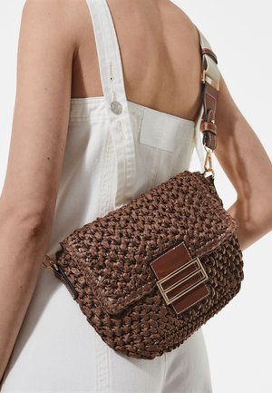 Hnědá tkaná taška s texturovaným povrchem, vybavená lesklou hnědou koženou klopou a zlatým kovovým dvojitým zapínáním na přezku.