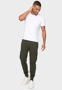 Camiseta blanca de manga corta combinada con pantalones joggers cargo verdes oliva que cuentan con bolsillos laterales y un cordón, completados con zapatillas blancas.