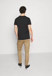 Černé tričko a khaki cargo kalhoty s více kapsami. Kalhoty mají elastické manžety a model má na sobě černé tenisky.