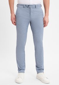 Lichtblauwe, slim-fit broeken gemaakt van gestructureerde stof met een subtiel patroon. Voorzien van een knoopsluiting en zijzakken. Draagt met witte sneakers.