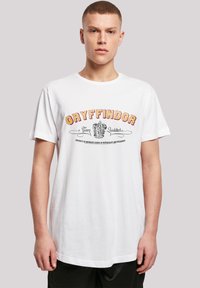 Hvit bomulls-T-skjorte med rød og gul "Gryffindor" tekst og et løveemblem, samt ekstra tekst i en vintage skrifttype. Vanlig passform, rund hals.