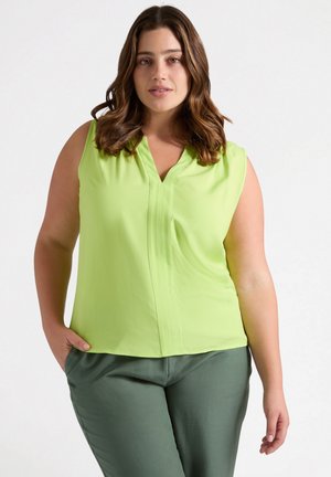 Blusa senza maniche verde chiaro con scollo a V, caratterizzata da dettagli plissettati. Abbinata a pantaloni verdi scuri, che mostrano una texture liscia.