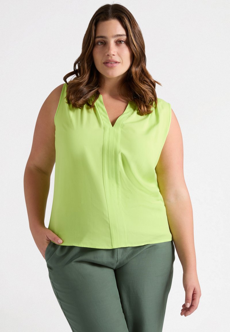 Blusa senza maniche verde chiaro con scollo a V, caratterizzata da dettagli plissettati. Abbinata a pantaloni verdi scuri, che mostrano una texture liscia.