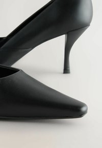 Mustat korkokengät, joissa on terävä kärki ja kiiltävä pinta. Kengissä on tyylikäs muotoilu ja ohuet, kapenevat stiletto-korkot.