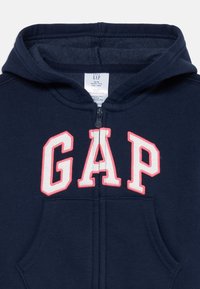 Felpa con cappuccio per neonati color blu navy, con zip frontale, tasca tipo kangaroo e logo "GAP" in bianco contornato di rosa sul petto.